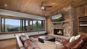 A spacious living room with a stone fireplace, leather sofas, and a large window offering a view of the outdoors. - Breakaway Ridge - Mountain Tops (Blue Ridge)