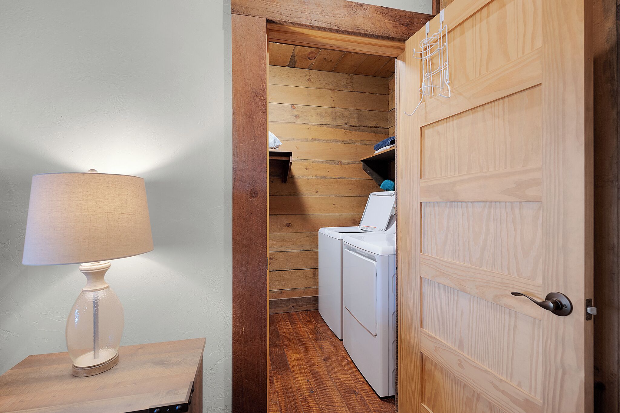Una lavanderia con una porta in legno, una lavatrice e una lampada su un tavolo di legno.
