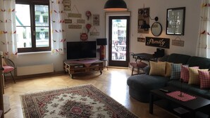 A living room with a television, sofa, and coffee table. There is a door leading outside, and the room has a rug and wall decorations. - Ferienwohnung 3 - Ferienwohnungen in der Kaffeewerkstatt (Sankt Wolfgang im Salzkammergut)