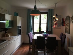 A kitchen with a dining table, chairs, a hanging light fixture, and a window with curtains.