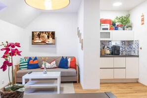 Un espace de vie compact comprenant un canapé, une table basse et un coin cuisine équipé d’un four à micro-ondes et d’une machine à café.