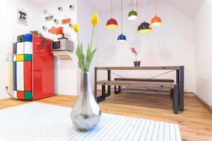 Une pièce avec un plancher en bois, une table à structure métallique, un meuble aux couleurs vives et un vase rempli de fleurs.