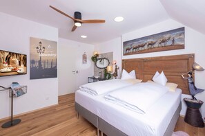 A modern bedroom with a large bed, a ceiling fan, a wooden headboard, and a wall-mounted painting.
