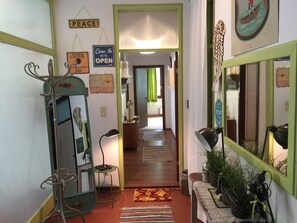A hallway with a green-framed mirror, a sign that says 'PEACE,' a 'Come In We're Open' sign, and a 'Beloved Home' sign.