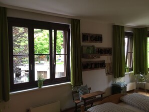 A room with a large window, a bench, a bed, and a wall-mounted shelf with decorative items.