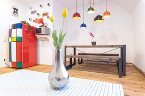 A room with a wooden floor, a metal-framed table, a colorful cabinet, and a vase with flowers.