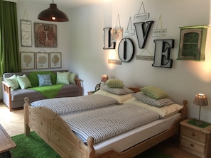 Une chambre à coucher avec un lit en bois, deux tables de chevet, une commode, un canapé vert et un mur orné d’affiches motivantes.