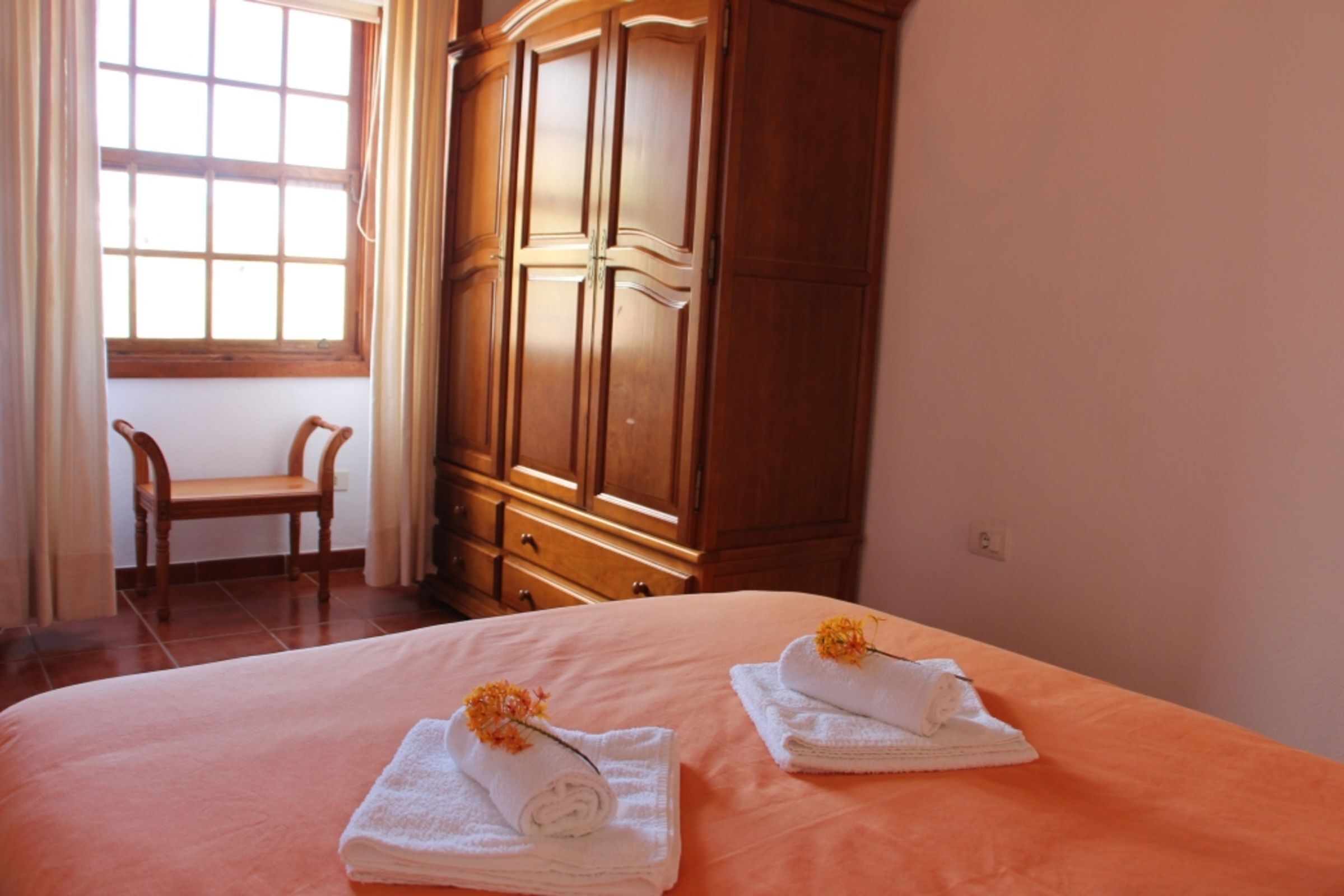 Ein Schlafzimmer mit einem Bett, zwei blumigen Handtüchern, einem Holzschrank, einem Stuhl und einem Fenster.