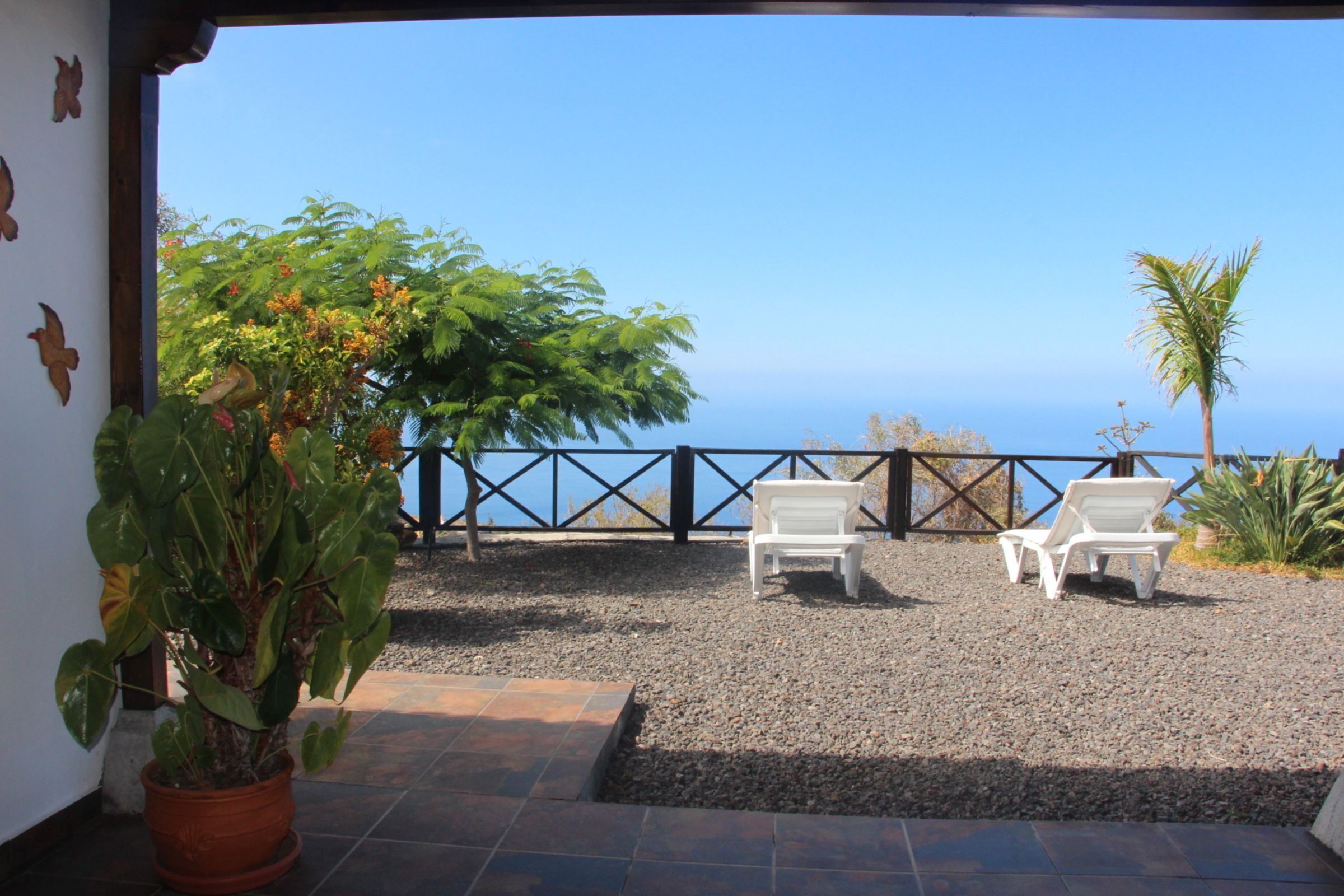A patio with two white lounge chairs, a potted plant, and a view of the ocean.