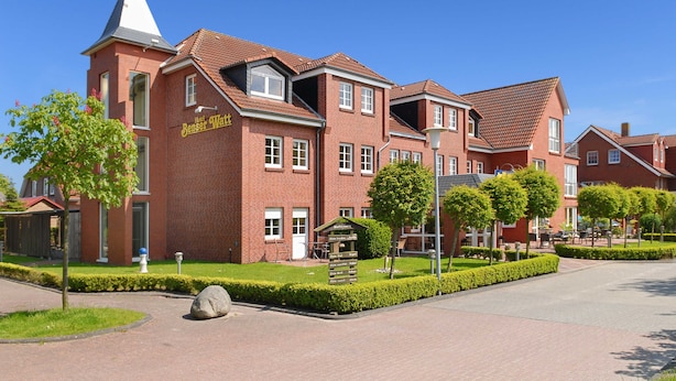 A red-brick hotel with a tower, a signboard, and a well-maintained garden.