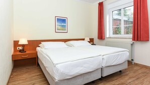 A double bed with a wooden headboard, two bedside tables with lamps, a window with red curtains, and a framed picture on the wall.