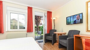 A hotel room with a bed, two armchairs, a small table, a TV, and a window with curtains.