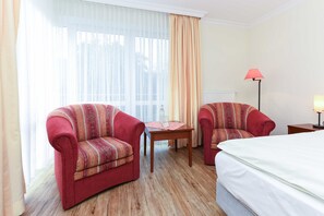 Ett hotellrum med två fåtöljer, ett litet bord, en lampa och en säng.