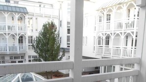 A balcony with a table set for two, chairs, and a view of a white building with balconies.
