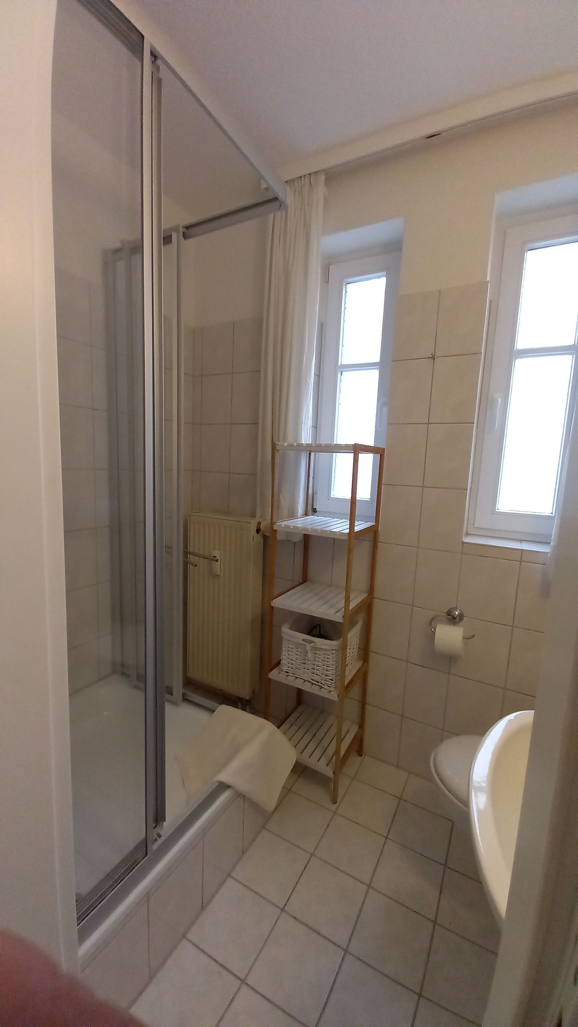 Ett badrum med en duschavdelning med glasväggar, en hylla i trä, ett element och ett fönster.