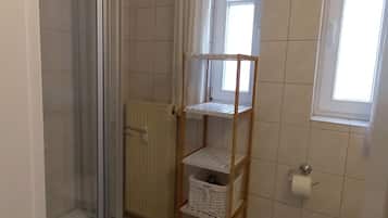Ett badrum med en duschavdelning med glasväggar, en hylla i trä, ett element och ett fönster.