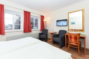 Une chambre d’hôtel avec un lit, deux chaises, un bureau, une télévision et une fenêtre avec des rideaux.
