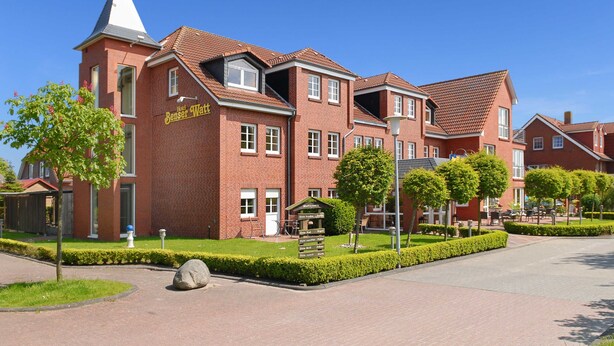 A red-brick hotel with a tower, a signboard, and a well-maintained garden.