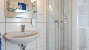 A bathroom with a white sink, a glass shower enclosure, and a mirror with lights.