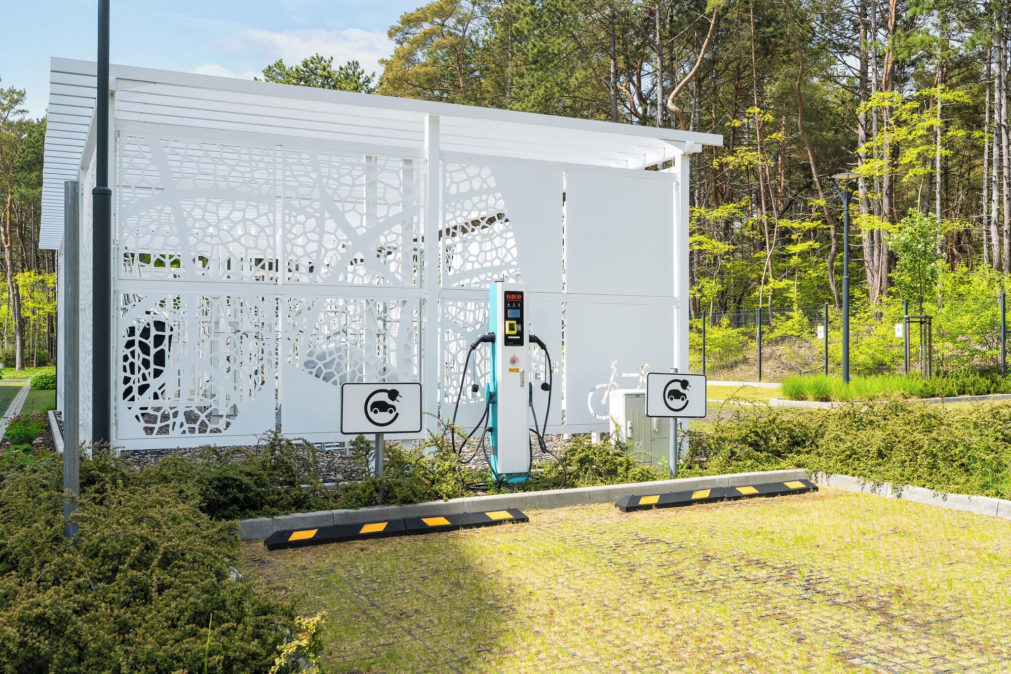 Una stazione di ricarica per veicoli elettrici con display digitale, immersa nel verde e alberi.