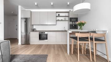 A modern kitchen with stainless steel appliances, a built-in oven, and a dining area with wooden chairs and a white table.
