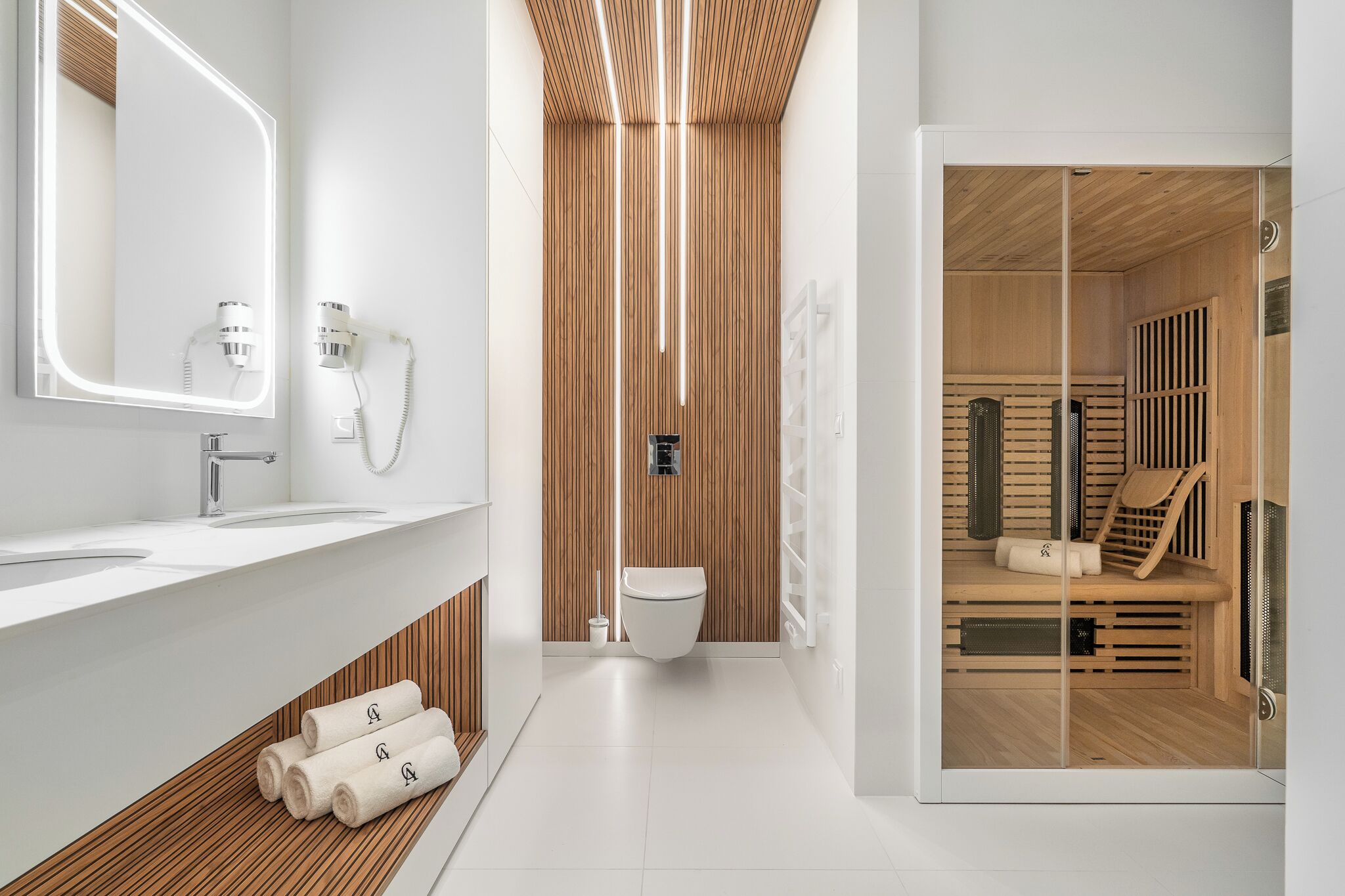 A modern bathroom with a white vanity, a large mirror, a toilet, and a sauna area visible through a glass door.
