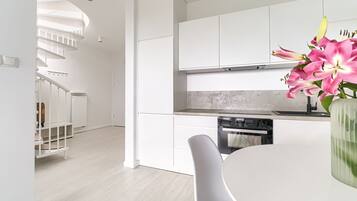 Una cocina moderna con armarios blancos, horno empotrado y comedor con mesa y silla blancos.