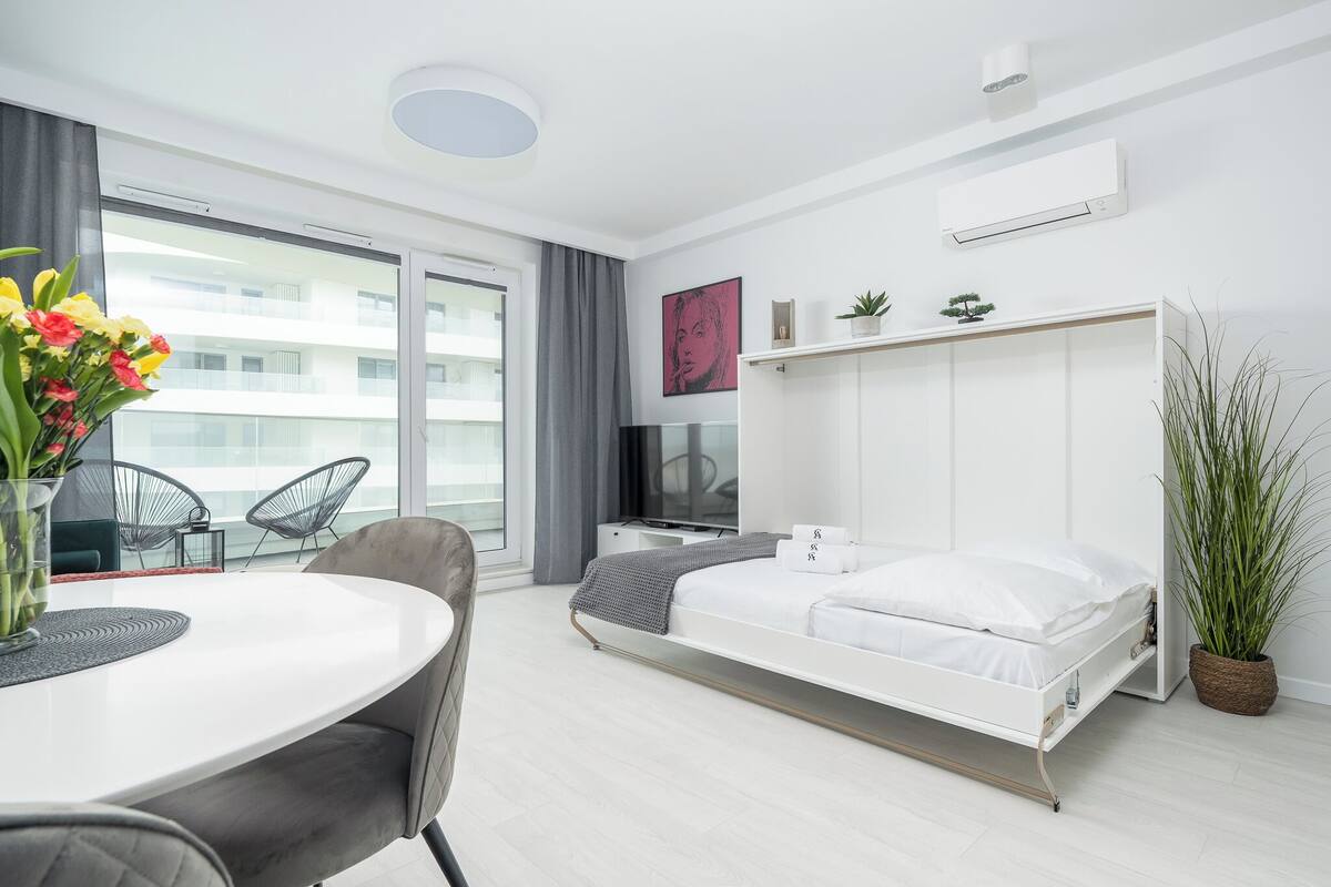 Habitació d'hotel moderna amb llit, escriptori, cadira, taula de menjador i una finestra gran.
