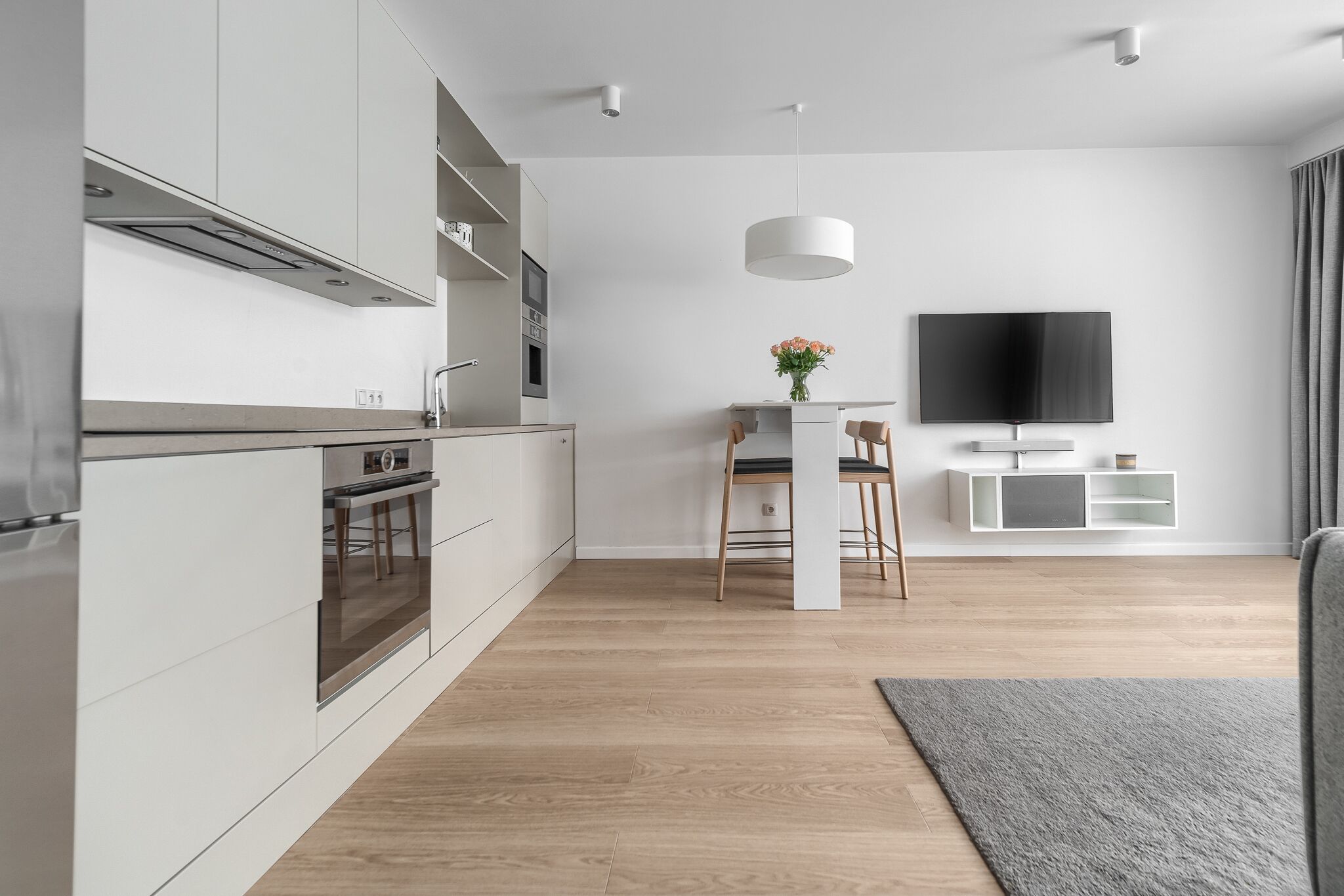 Eine moderne Küche mit eingebauten Geräten, ein Essbereich mit Fernseher und ein grauer Teppichboden.