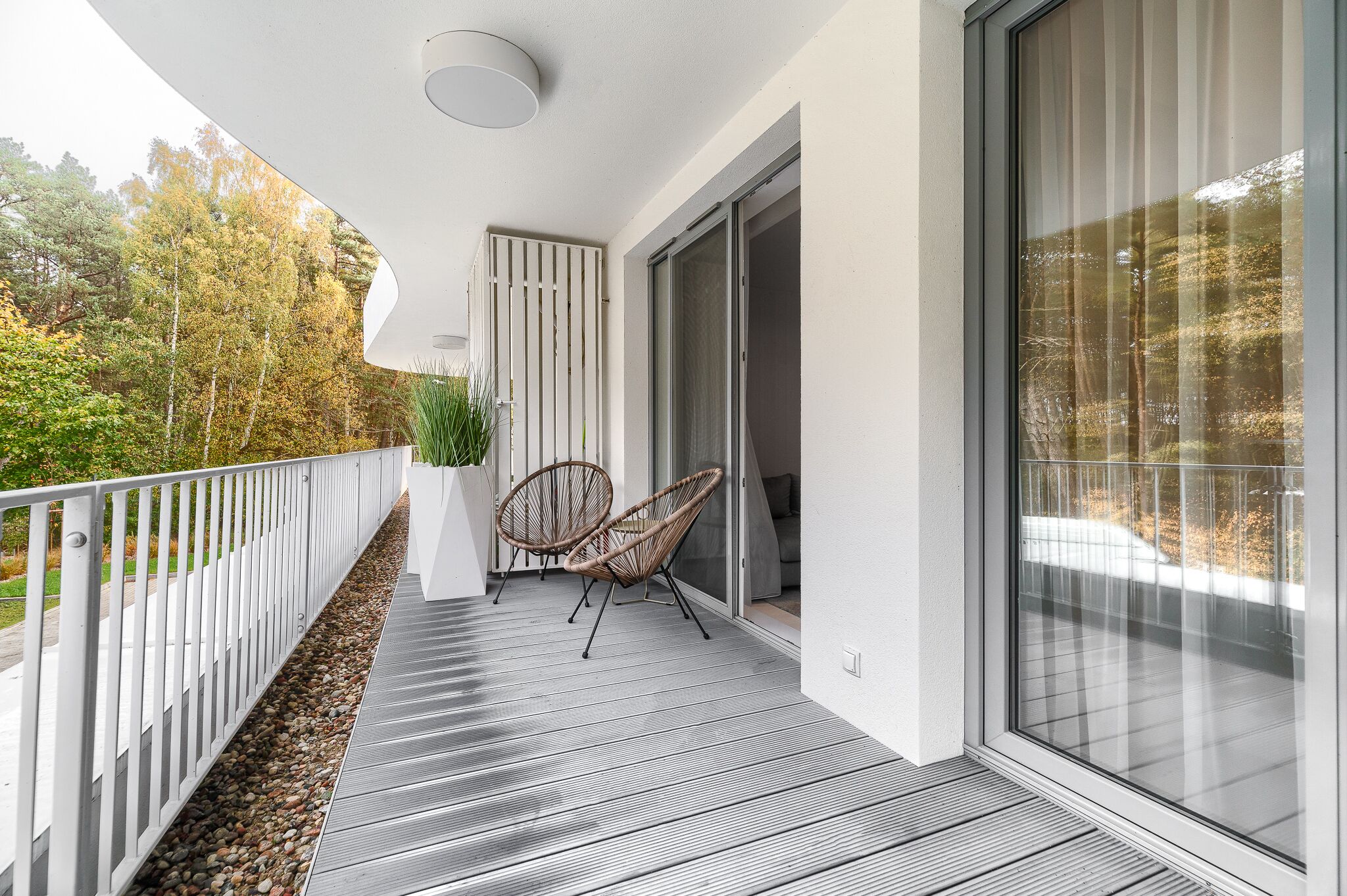 Ein Balkon mit Holzboden, weißer Geländer und zwei Korbstühlen.