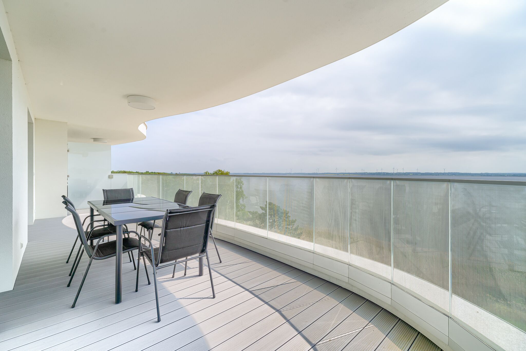 Un balcon avec une table et des chaises, donnant sur une étendue d’eau et sur des bâtiments situés au loin.