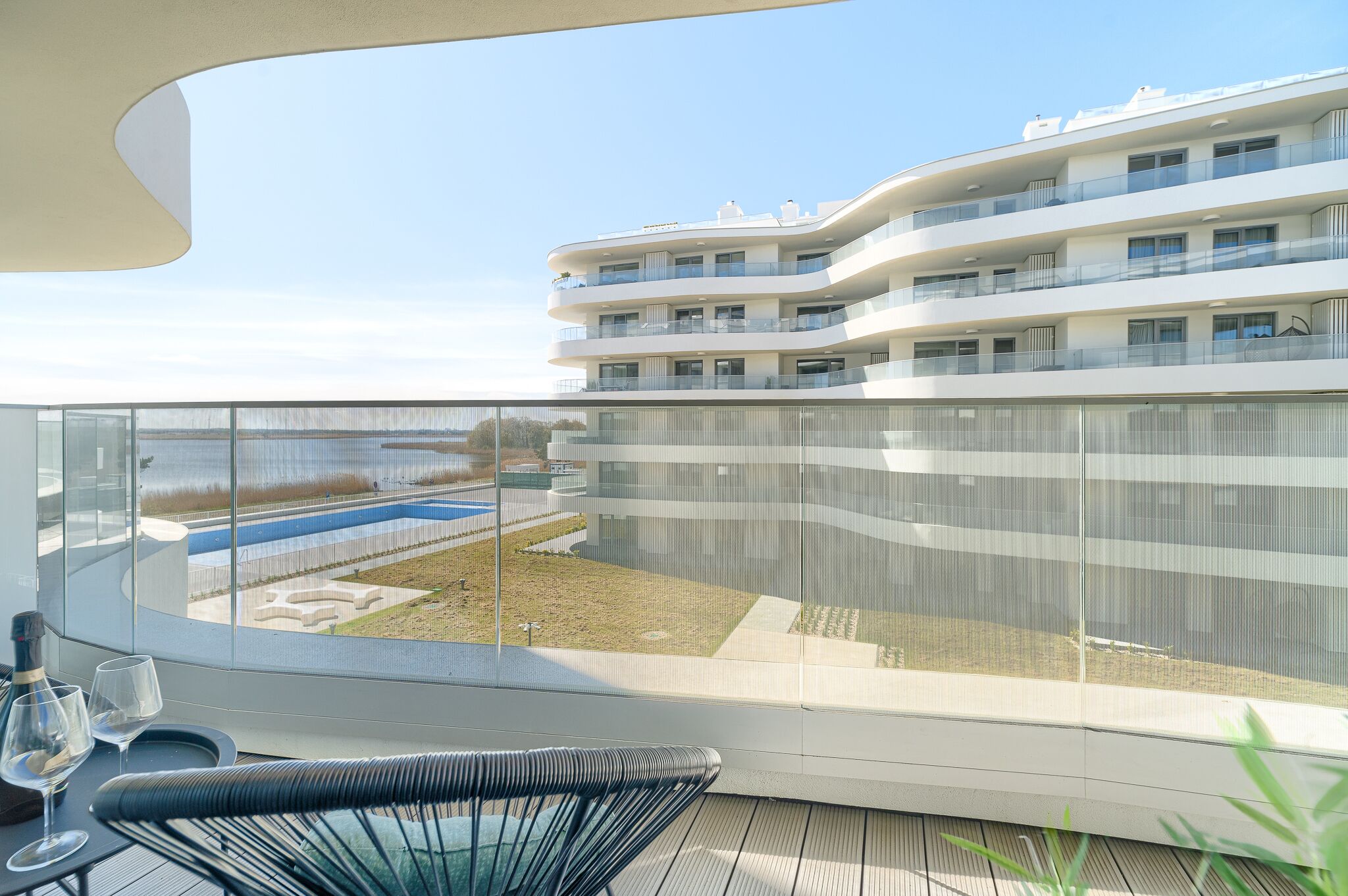 A modern apartment with a balcony overlooking a pool and a landscaped area.