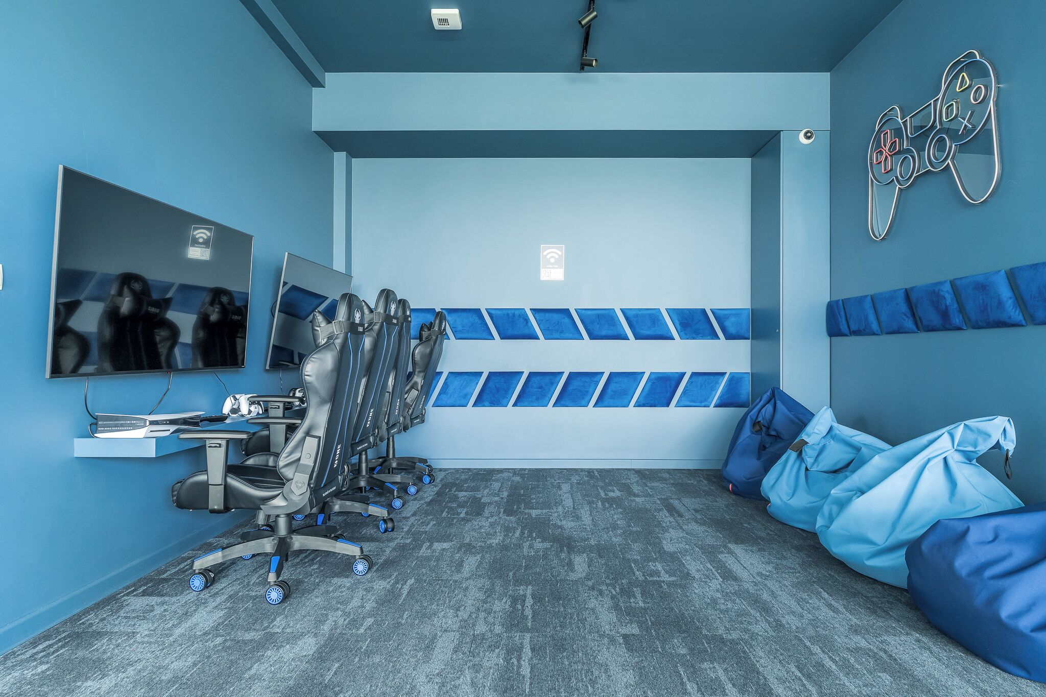 A room with a gaming chair, a desk with a computer, a wall-mounted TV, and a gaming controller decoration.