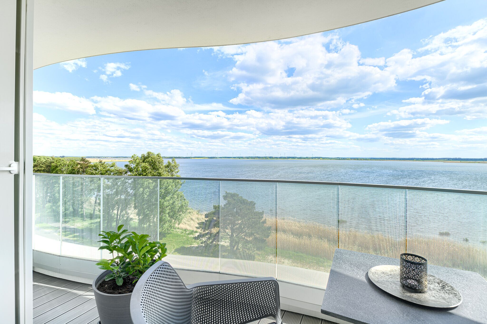 A balcony with a view of a lake, a potted plant, and a table with a decorative item.