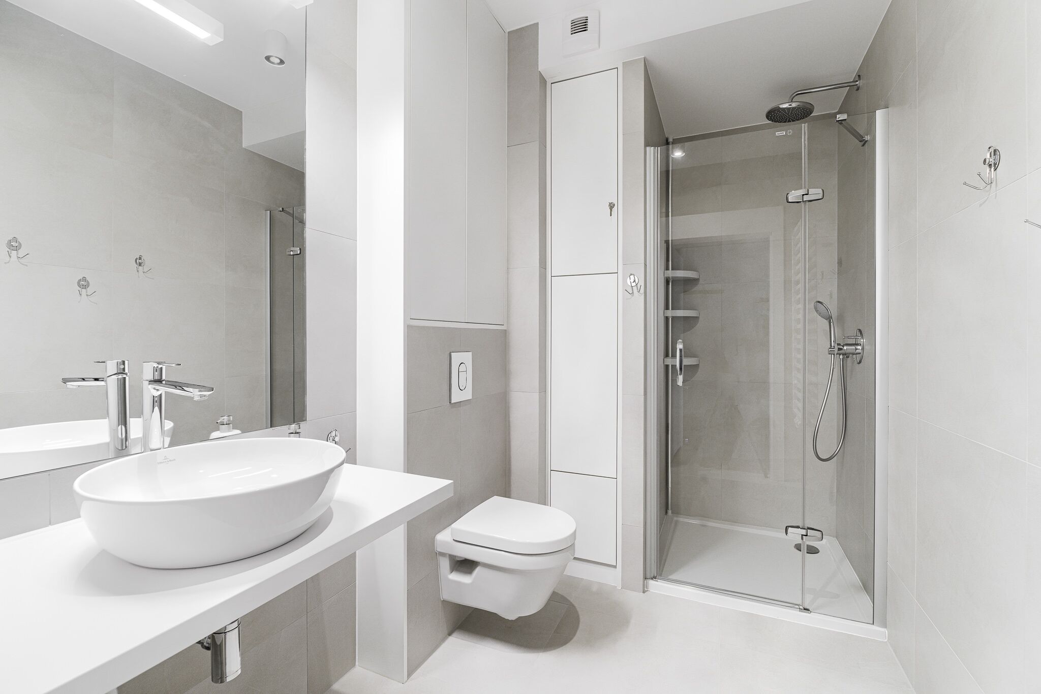 A modern bathroom with a large white sink, a toilet, and a glass-enclosed shower area.