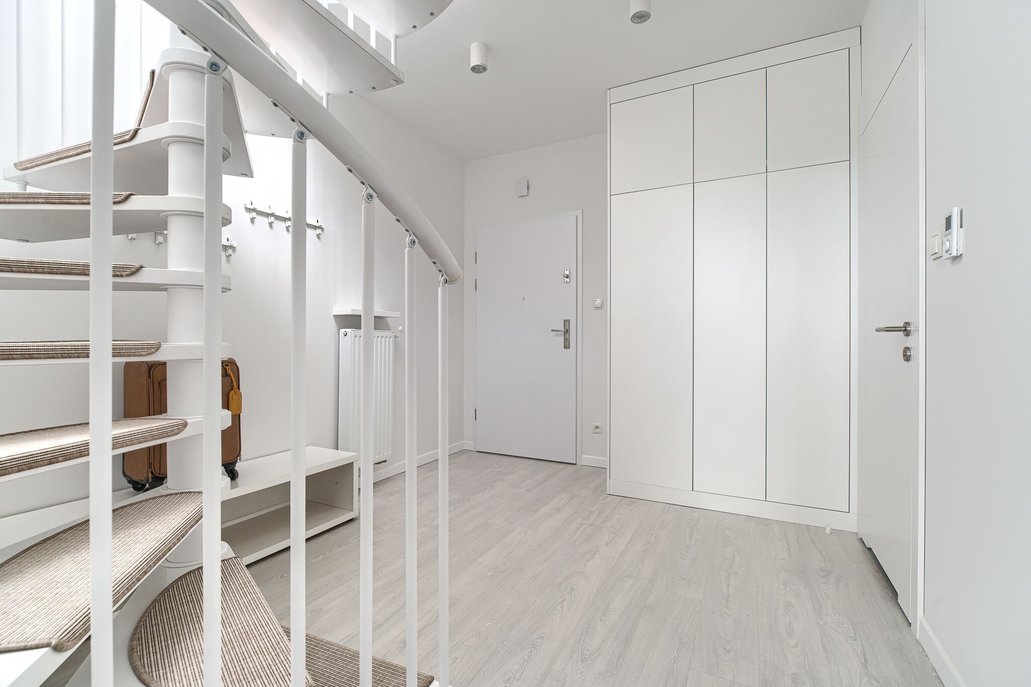 A modern, minimalist room with a staircase, built-in shelves, and a large wardrobe.