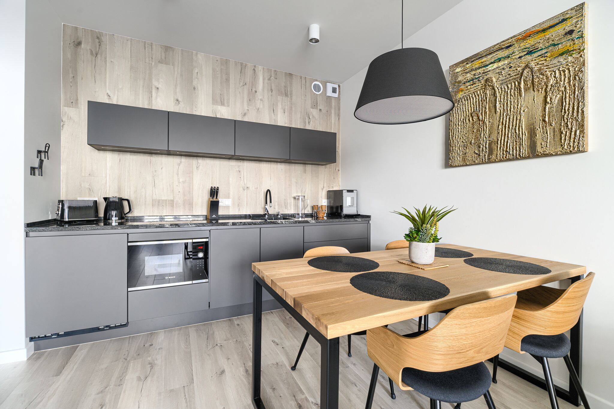A modern kitchen with grey cabinets, a wooden countertop, and a dining area with a wooden table and chairs.