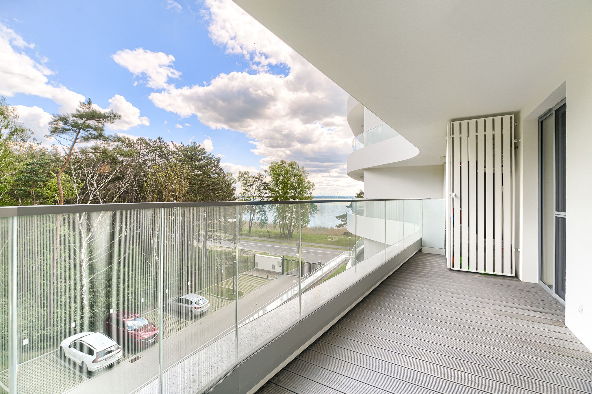 Un balcon moderne donnant sur un parking et des arbres.