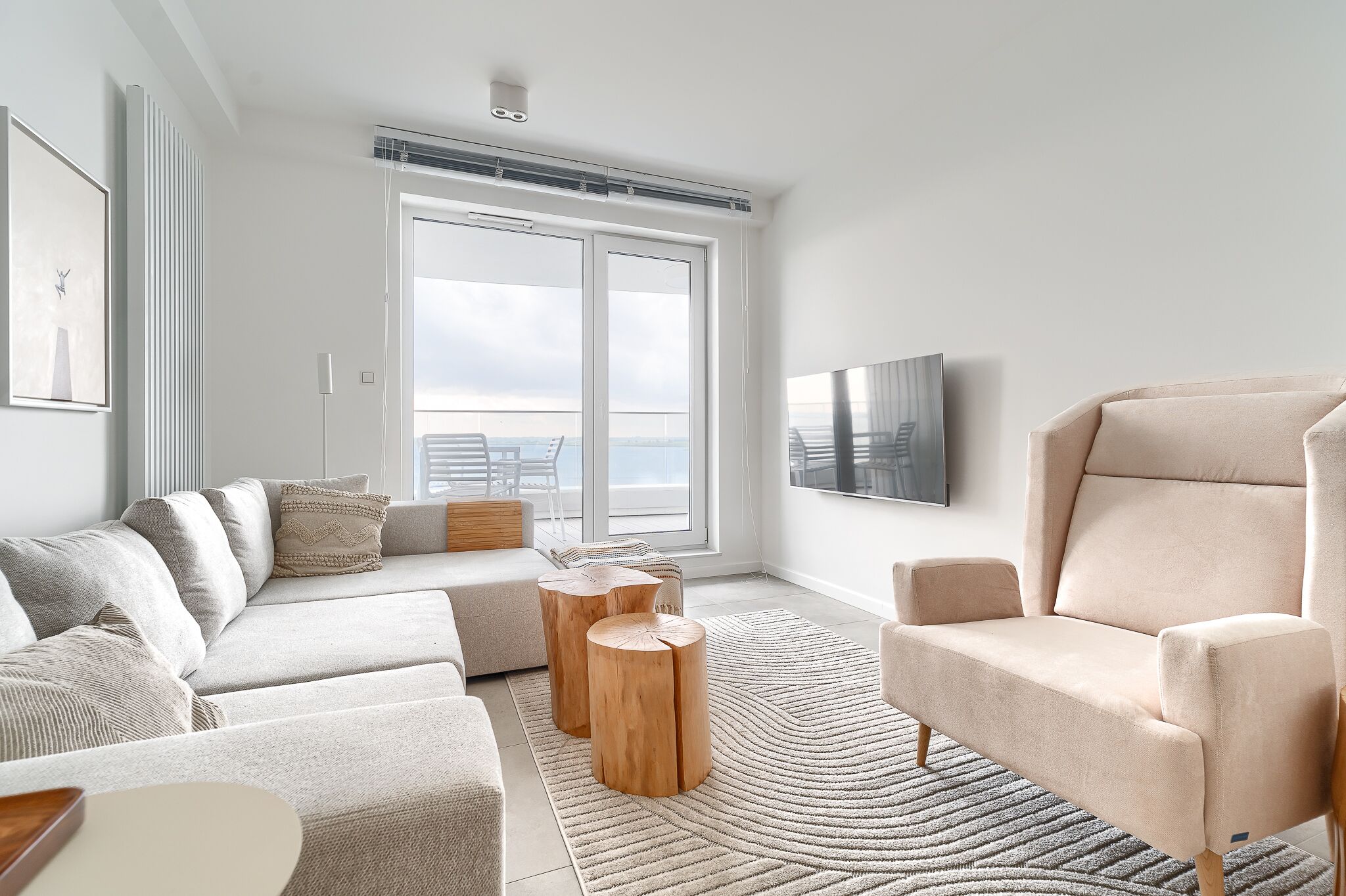 A modern living room with a sofa, armchair, and round wooden side tables.