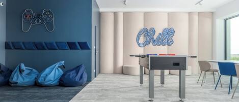 A modern room with a foosball table, blue bean bags, and a wall-mounted game controller.