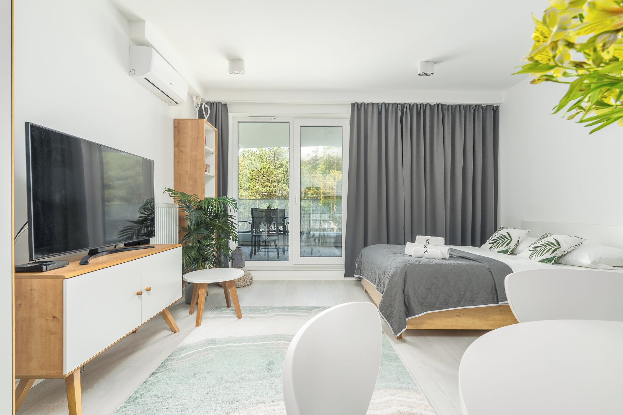A modern bedroom with a TV, a bed, a desk, and a balcony.