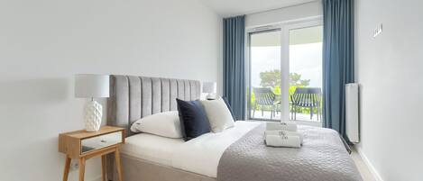 Un dormitorio moderno con cama, mesita de noche con lámpara, vista al exterior a través de un ventanal grande y aire acondicionado instalado en el techo.
