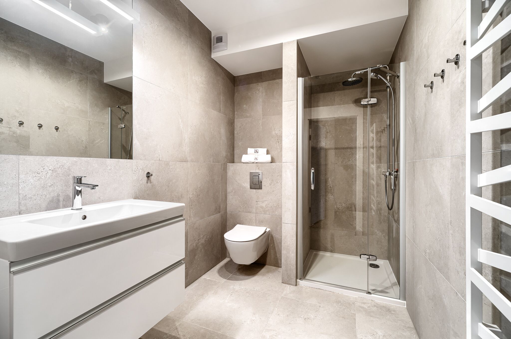 Un baño moderno con ducha de vidrio, inodoro independiente y un mueble de tocador espacioso con lavamanos.