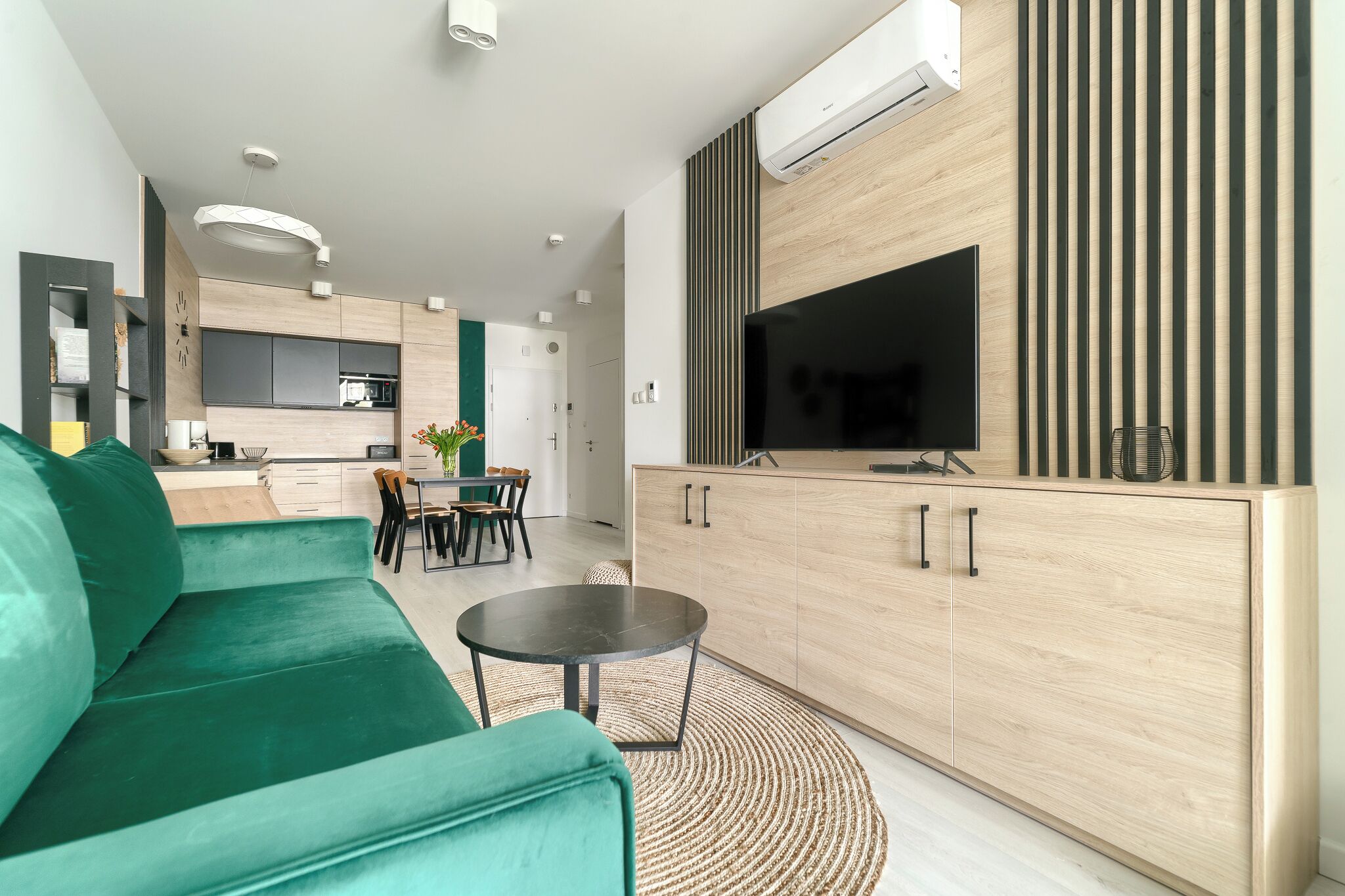 A modern living room with a green sofa, a round coffee table, and a TV mounted on a wooden cabinet.