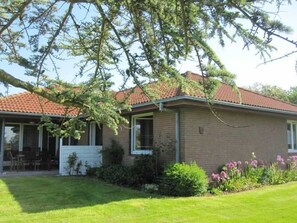 A single-story brick house with a red-tiled roof, a covered porch, and a well-maintained lawn.