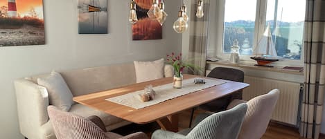 Un comedor con mesa de madera, sillas acolchadas y vista a un paisaje urbano a través de una ventana.