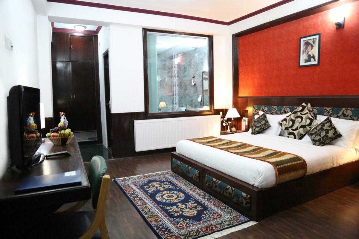 Habitación de hotel con cama, escritorio con computadora, silla, ventana con vista y pared de acento roja.