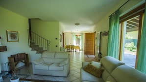 En rummelig stue med sofa, sofabord og trappe op til et andet værelse.