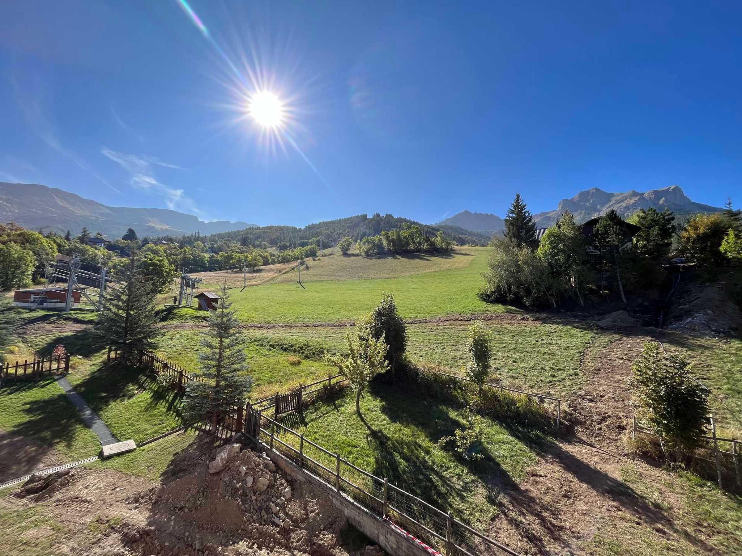 Un paysage montagneux, avec un ciel dégagé, une zone délimitée par une clôture et une chaîne de montagnes à l’horizon.