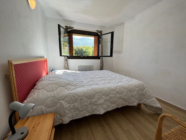 Et soveværelse med seng, skrivebord, stol, vindue med udsigt til bjerge og en radiator.
